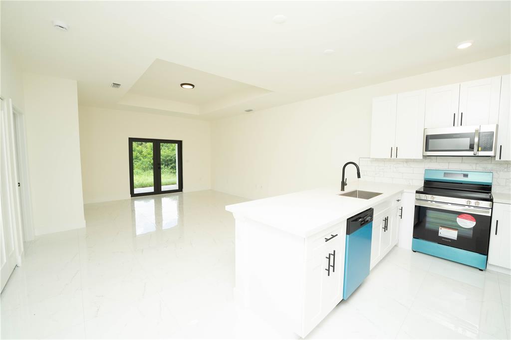 A modern kitchen with white cabinets and a central island opens to a living area — 4706 27TH STREET SW, LEHIGH ACRES, FL