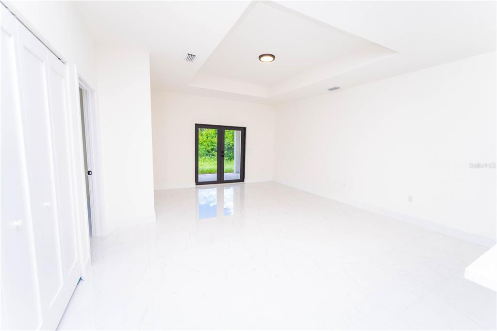 A bright, empty room with white tile floors, a tray ceiling, and glass double doors — 4706 27TH STREET SW, LEHIGH ACRES, FL