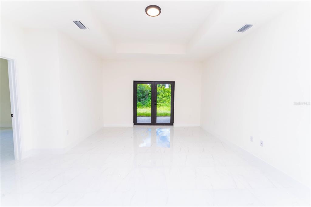 An empty room with white tile floors, a tray ceiling, and double glass doors — 4706 27TH STREET SW, LEHIGH ACRES, FL