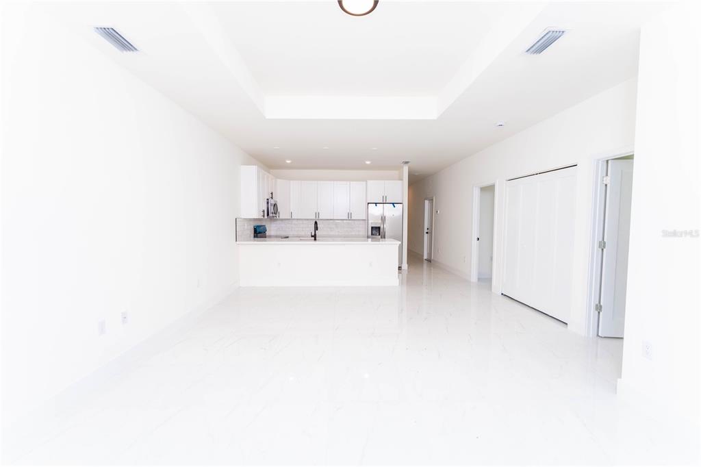 A bright, open-concept kitchen and living area features white cabinetry, stainless appliances, and tile flooring — 4706 27TH STREET SW, LEHIGH ACRES, FL