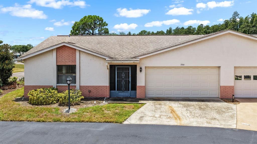 A single-story house with a beige stucco exterior, brick accents, and a two-car garage — 1760 ATRIUM DRIVE, SUN CITY CENTER, FL