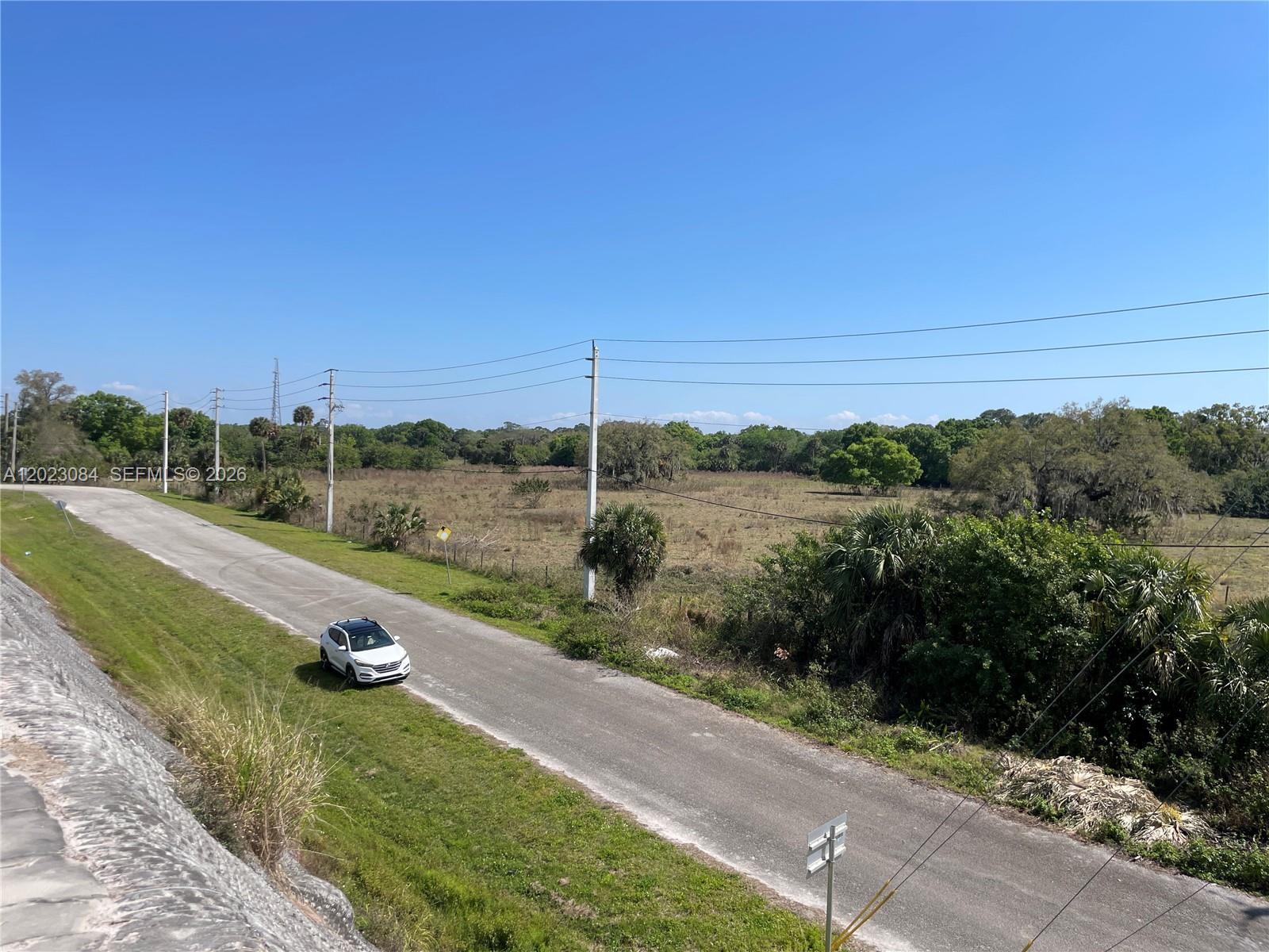 A white car drives along a paved road bordering a large, grassy, undeveloped field — 2358 E SR 70, Okeechobee FL 34972, OKEECHOBEE, FL
