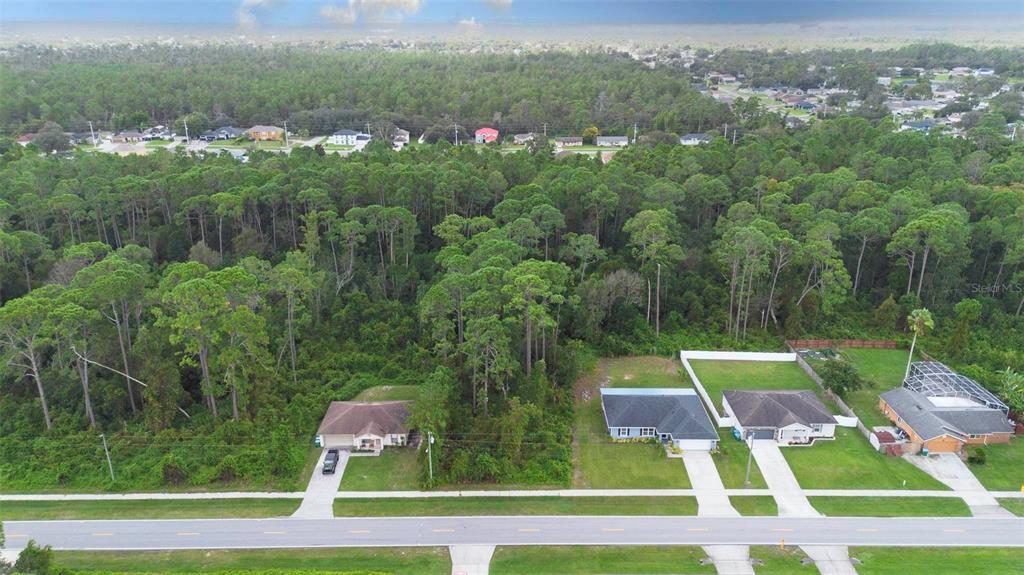 An aerial view shows three suburban houses situated along a road bordering a dense forest — 2657 CAPTAIN DRIVE, DELTONA, FL
