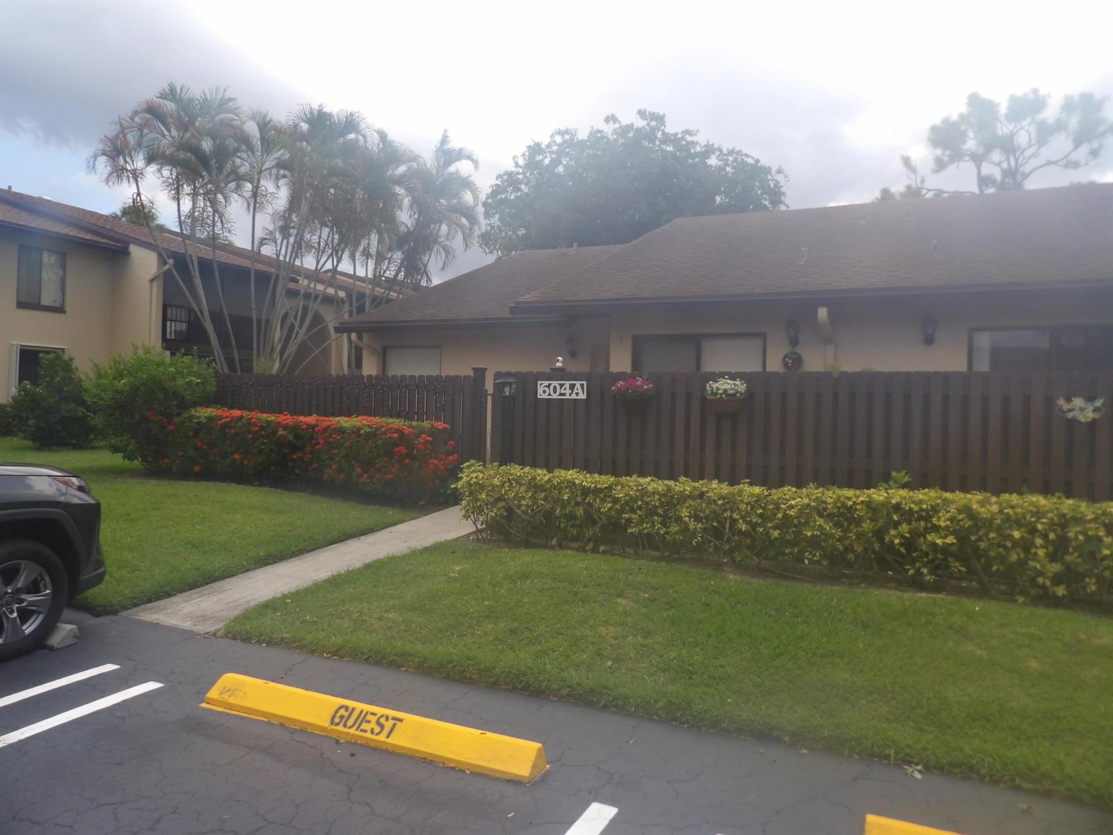 A single-story residence with a brown fence, a guest parking space, and palm trees — 604 Sea Pine Way # A, FL 33415, FL