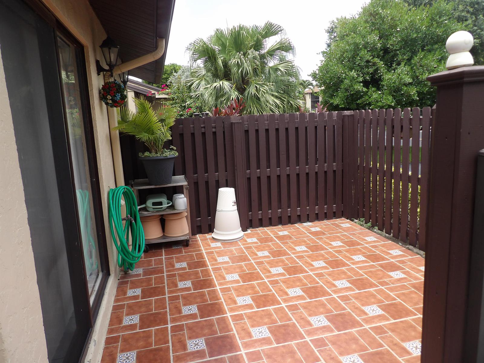 A patio features terracotta-colored tiles with decorative insets, a brown picket fence, and a hose — 604 Sea Pine Way # A, FL 33415, FL