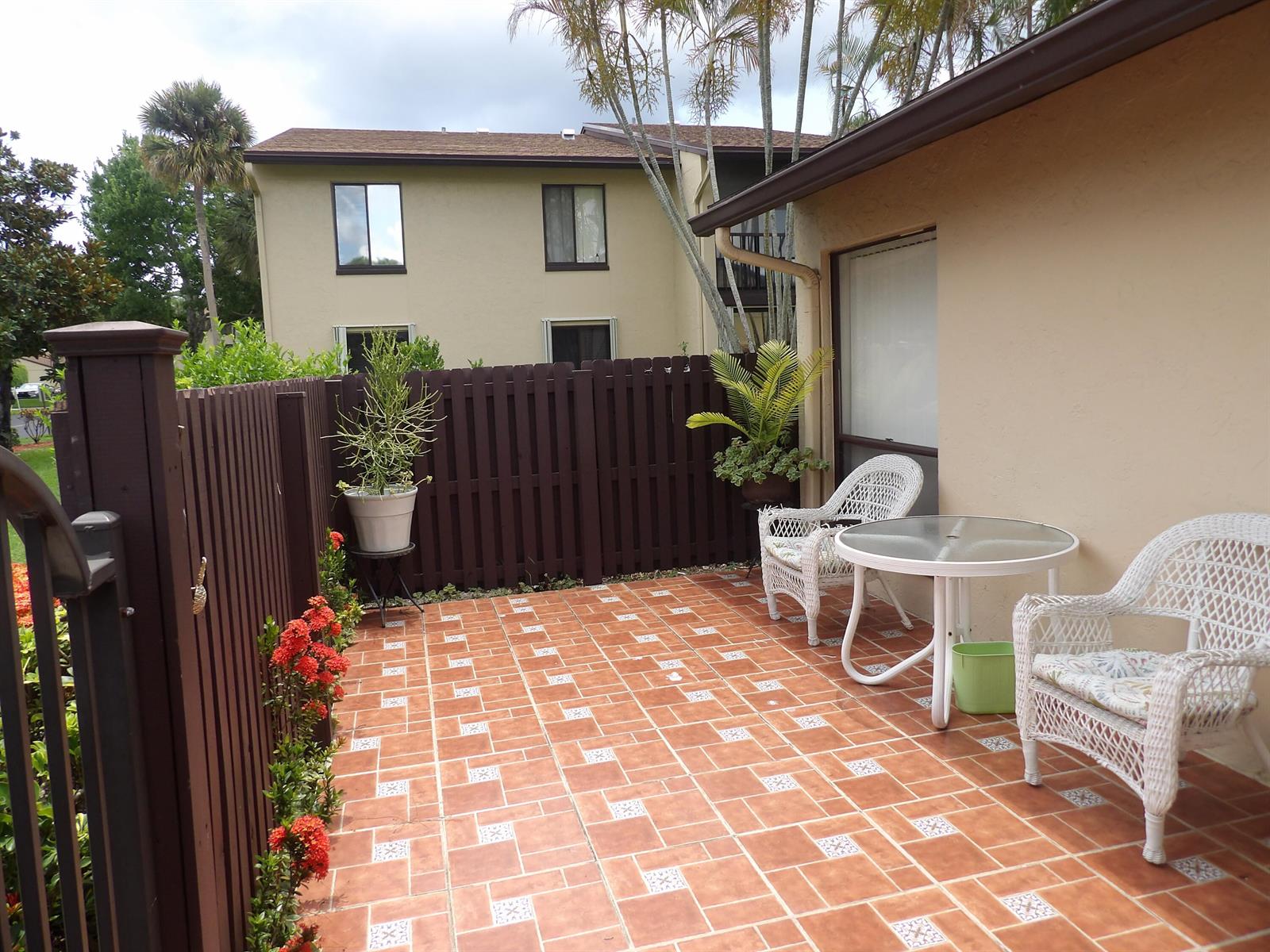 A patio with a tiled floor, two white wicker chairs, a table, and a wooden fence — 604 Sea Pine Way # A, FL 33415, FL