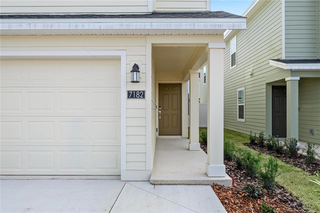 A beige house exterior features a garage, a covered entryway, and a brown front door — 7212 SW 91ST LANE, OCALA, FL