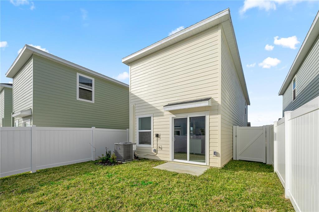 A backyard with a small concrete patio, a sliding glass door, and white vinyl fencing — 7212 SW 91ST LANE, OCALA, FL