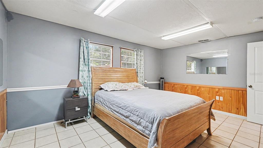 A bedroom features a wooden bed frame, tile flooring, gray walls, and wood wainscoting — 7075 W HOMOSASSA TRAIL, HOMOSASSA, FL