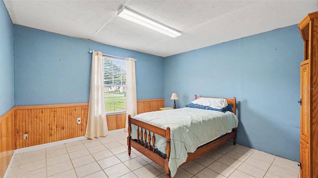 A bedroom with blue walls, wood wainscoting, tile flooring, and a single wooden bed frame — 7075 W HOMOSASSA TRAIL, HOMOSASSA, FL