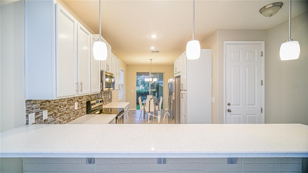 A kitchen features white cabinets, a stone backsplash, a breakfast bar, and stainless steel appliances — 2945 CELLO LANE, KISSIMMEE, FL