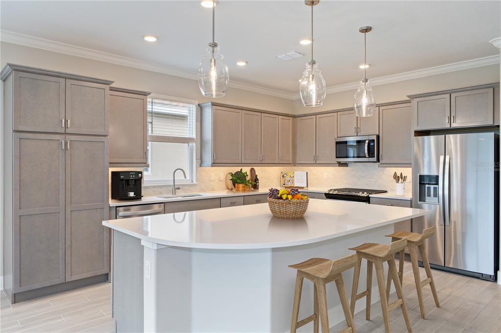 A modern kitchen features gray cabinets, a large white island, and stainless steel appliances — 4516 NW 54TH TERRACE, OCALA, FL