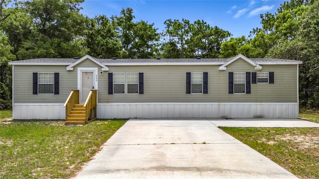 A single-story manufactured home with light green siding, dark shutters, and a concrete driveway — 6498 W ROSEDALE DRIVE, HOMOSASSA, FL