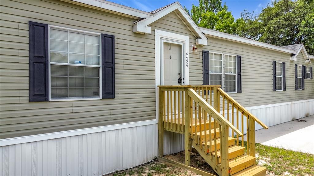 A tan mobile home exterior features a wooden staircase leading to the front entrance — 6498 W ROSEDALE DRIVE, HOMOSASSA, FL