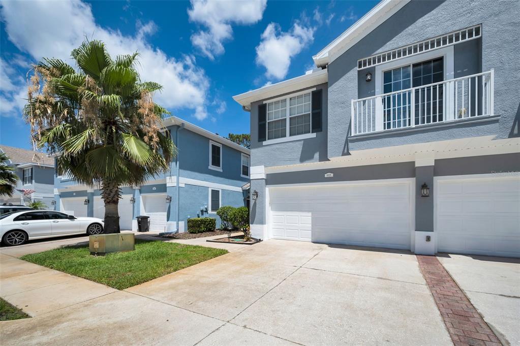A two-story blue townhouse with a white garage door, balcony, and a palm tree — 8525 SHALLOW CREEK, NEW PORT RICHEY, FL