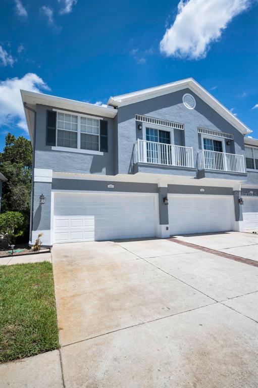 A two-story townhouse exterior features gray stucco siding, white garage doors, and upper-level balconies — 8525 SHALLOW CREEK, NEW PORT RICHEY, FL