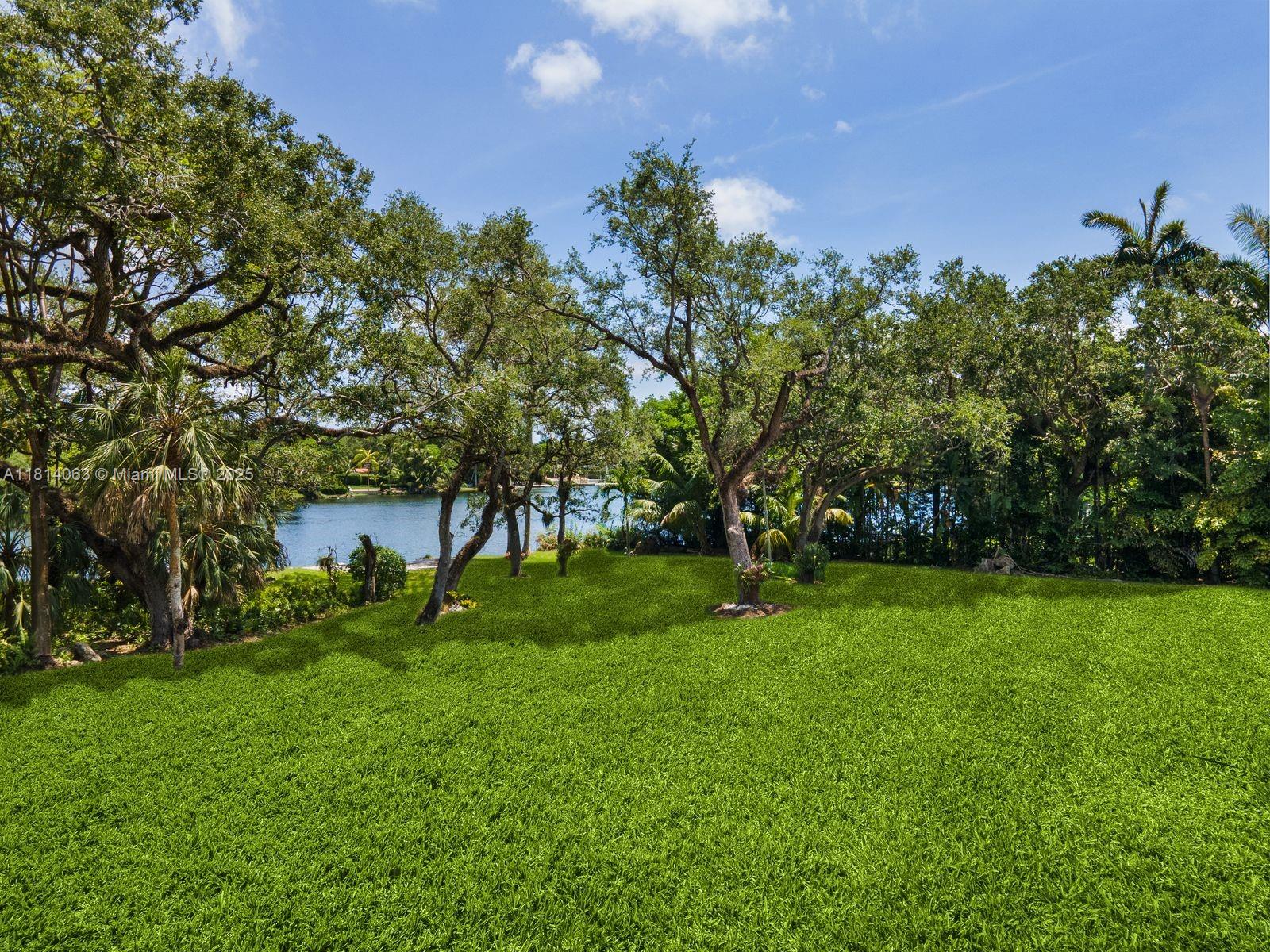 A grassy backyard features mature trees and a view of a lake — 5355 Hammock Dr, Coral Gables FL 33156, CORAL GABLES, FL