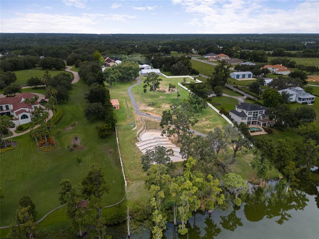 An aerial view shows a large grassy lot with a terraced stone amphitheater near a lake — 11901 FORT KING HIGHWAY, THONOTOSASSA, FL