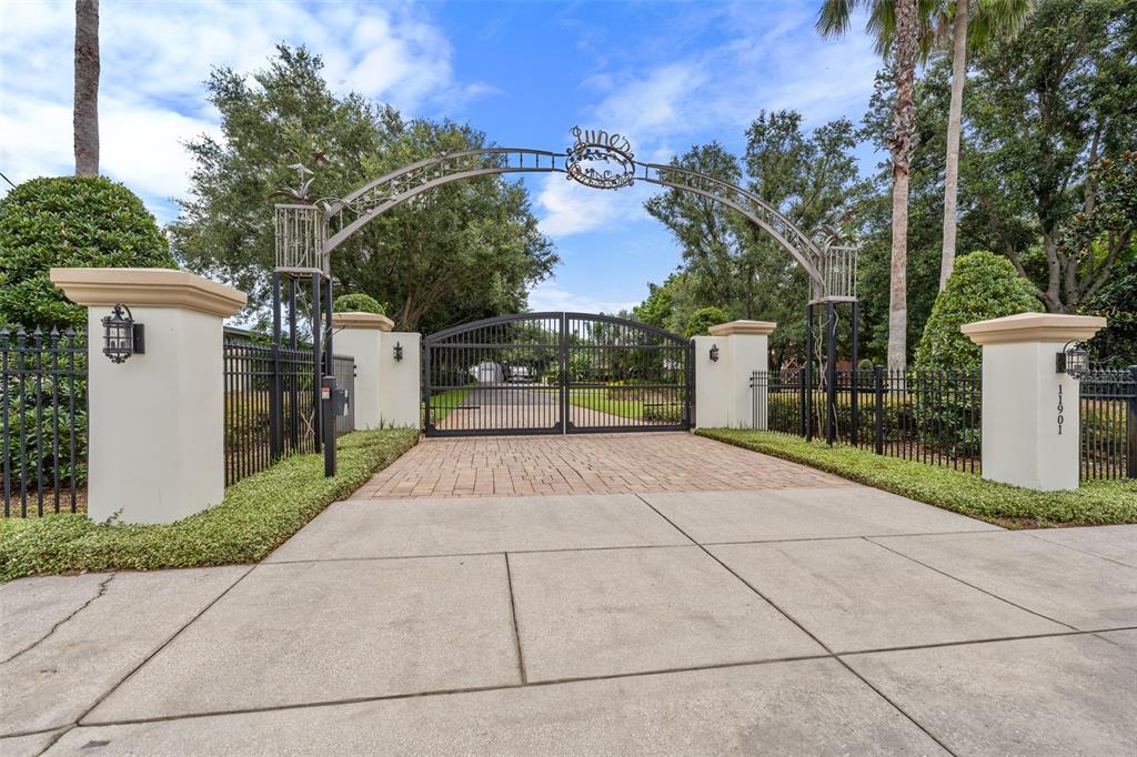 A gated entrance with a metal archway and stone pillars leads to a paved driveway — 11901 FORT KING HIGHWAY, THONOTOSASSA, FL