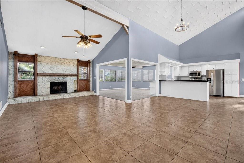 A staged living room with a stone fireplace, vaulted ceilings, and an open kitchen area — 112 ALBATROSS WAY, DAYTONA BEACH, FL