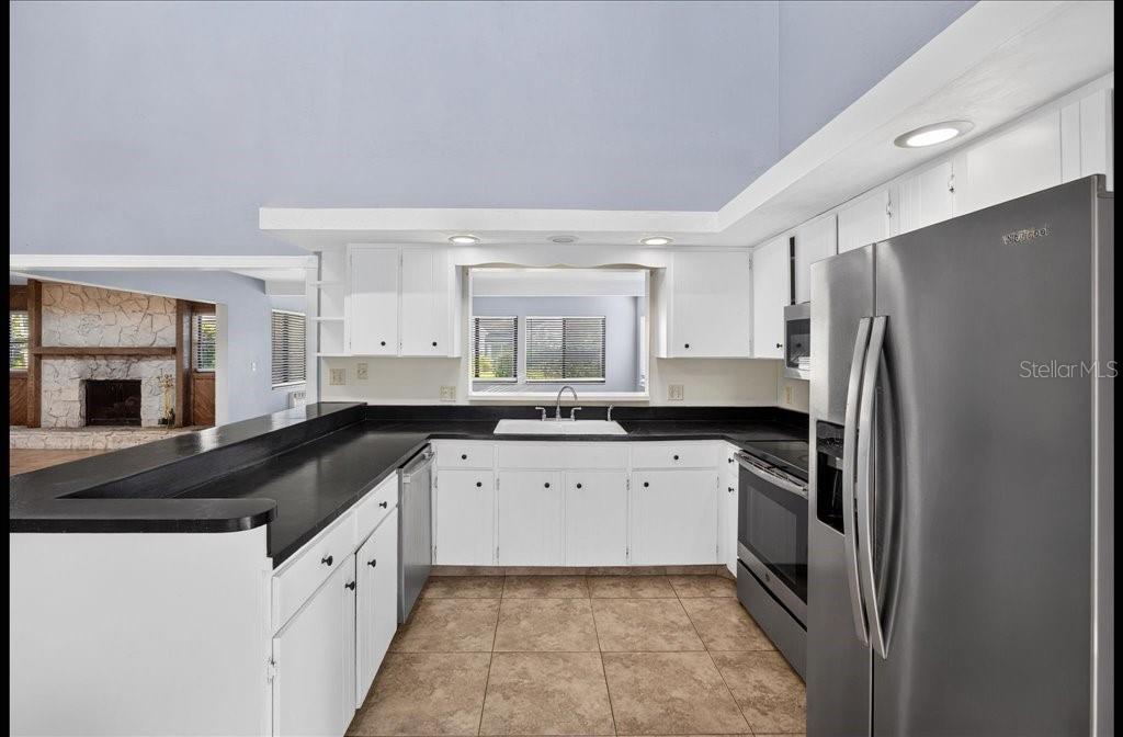 An open-concept living room and kitchen feature vaulted ceilings, tile flooring, and a stone fireplace — 112 ALBATROSS WAY, DAYTONA BEACH, FL
