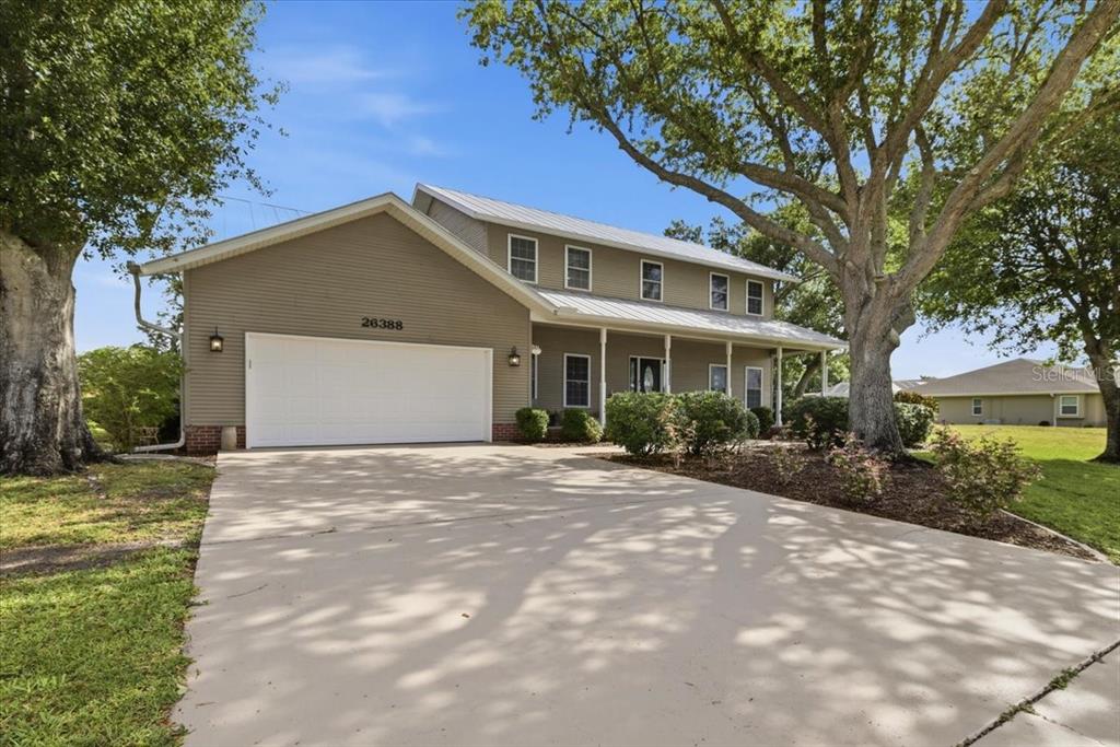 A two-story house with tan siding, a metal roof, and a large concrete driveway — 26388 HONG KONG ROAD, PUNTA GORDA, FL