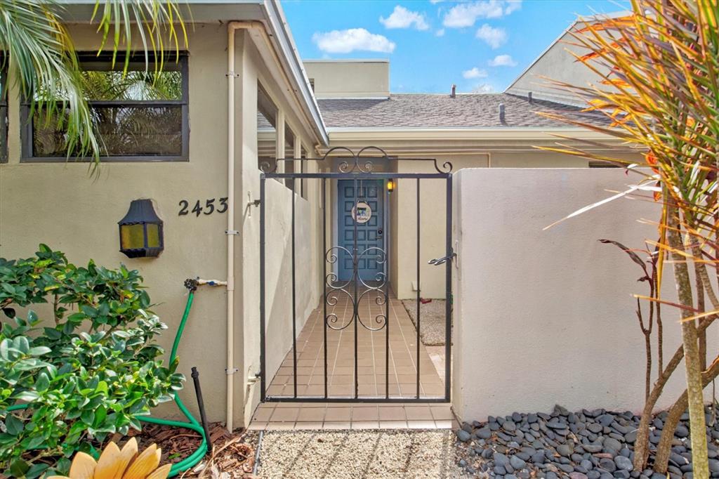 A gated courtyard entrance leads to a blue front door of a tan stucco home — 2453 CRISPIN COURT UNIT F4, SARASOTA, FL