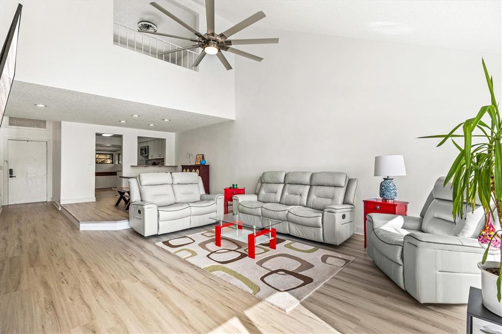 A living room features light wood flooring, a high ceiling with a fan, and gray furniture — 2453 CRISPIN COURT UNIT F4, SARASOTA, FL