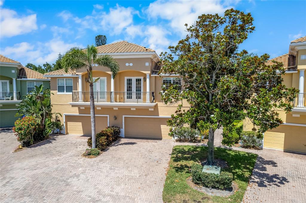 A two-story tan stucco house features a balcony, two garage doors, and a paved driveway — 191 BANYAN BAY DRIVE, ST PETERSBURG, FL