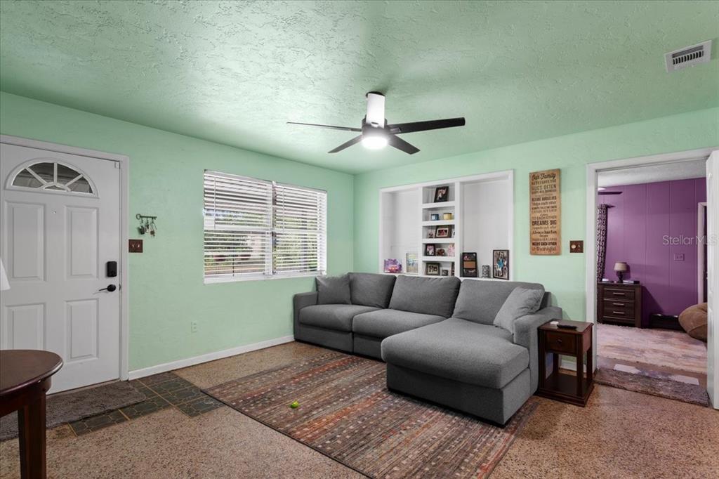 A living room features mint green walls, a gray sectional sofa, and built-in wall shelving — 1636 NW 34TH PLACE, GAINESVILLE, FL