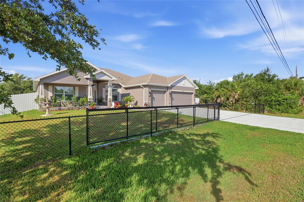 A single-story house with a tan exterior, a two-car garage, and a black chain-link fence — 14735 KEYSTONE BOULEVARD, PORT CHARLOTTE, FL