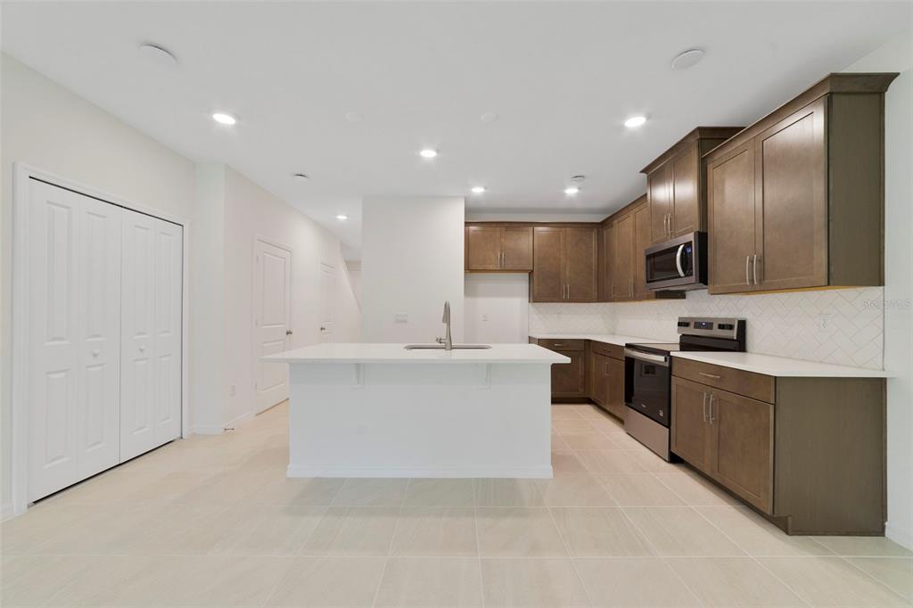 A kitchen features brown cabinets, white countertops, a central island, and light-colored tile flooring — 1661 GREENLEAF WOODS COVE, OVIEDO, FL