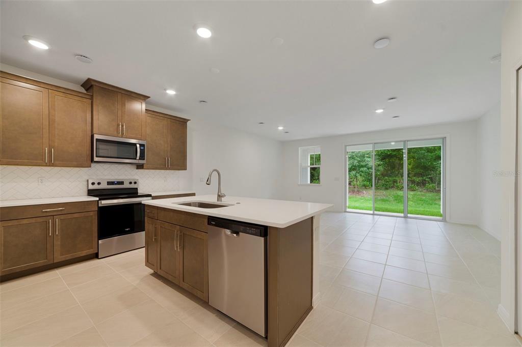 A kitchen with brown cabinets, stainless steel appliances, and an island overlooks a sliding door — 1661 GREENLEAF WOODS COVE, OVIEDO, FL