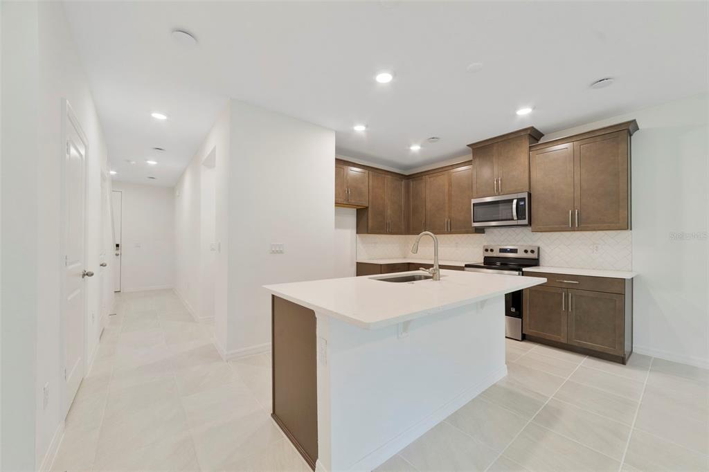 A modern kitchen features brown cabinets, white countertops, a central island, and light tile flooring — 1661 GREENLEAF WOODS COVE, OVIEDO, FL
