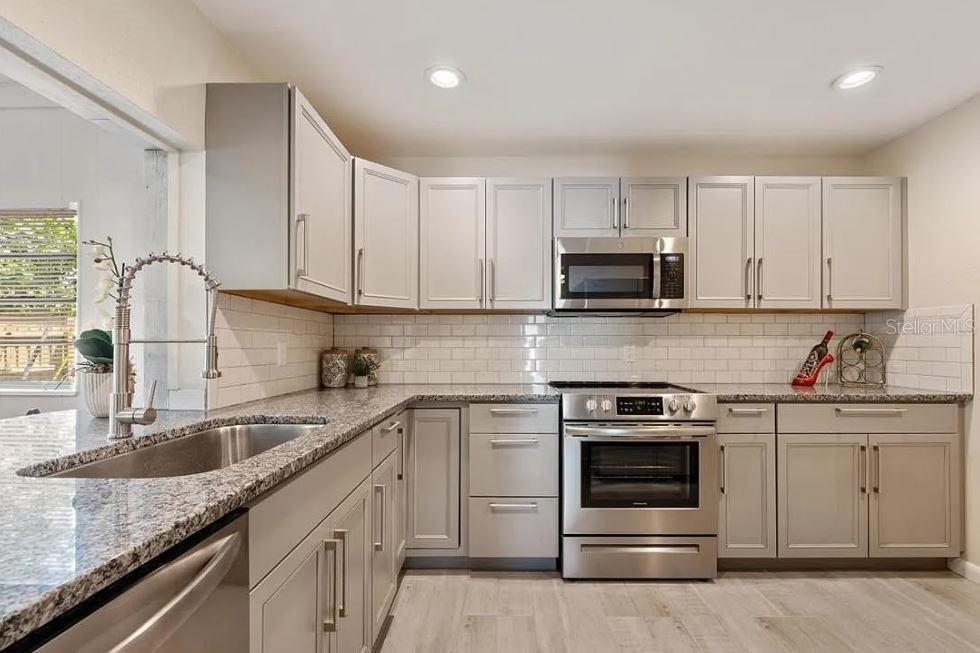 A kitchen features light gray cabinets, granite countertops, stainless steel appliances, and a white backsplash — 4325 ELLIOT AVENUE, TITUSVILLE, FL