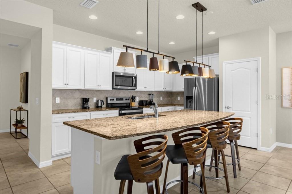 A kitchen features white cabinets, granite countertops, a large island with bar stools, and pendant lighting — 2413 DUBAI ST, KISSIMMEE, FL