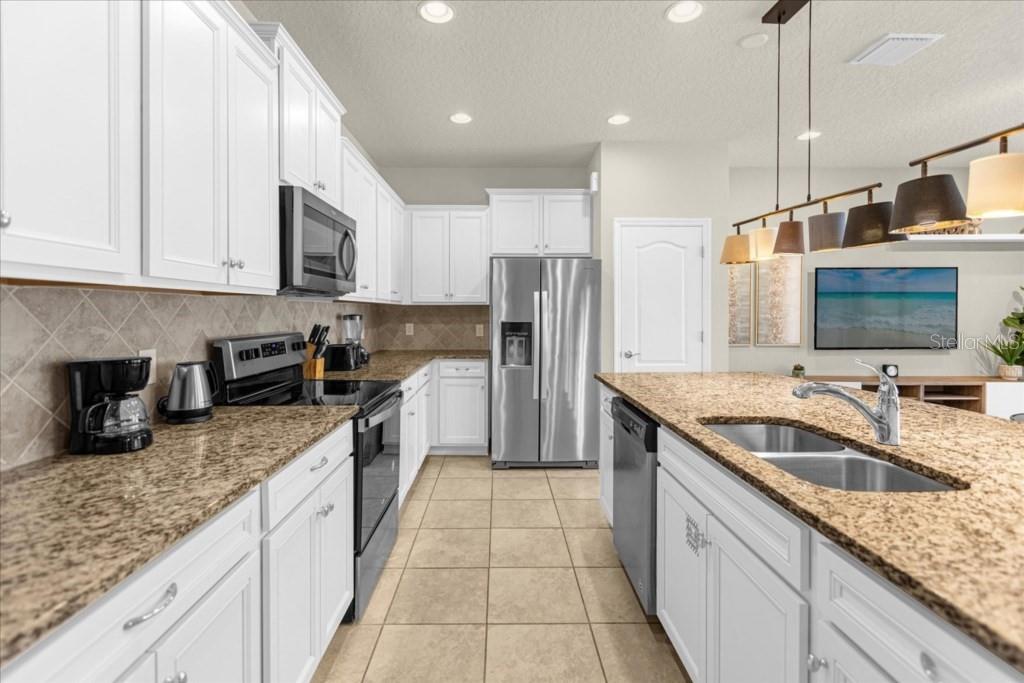 A kitchen features white cabinets, granite countertops, stainless steel appliances, and a central island — 2413 DUBAI ST, KISSIMMEE, FL