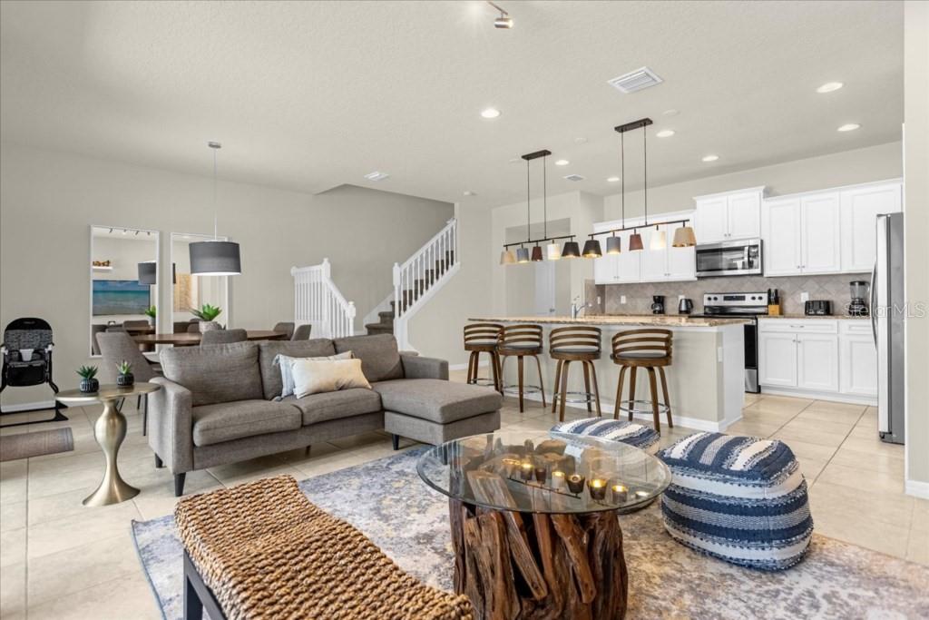 An open-concept living room and kitchen featuring a gray sectional, island seating, and white cabinets — 2413 DUBAI ST, KISSIMMEE, FL