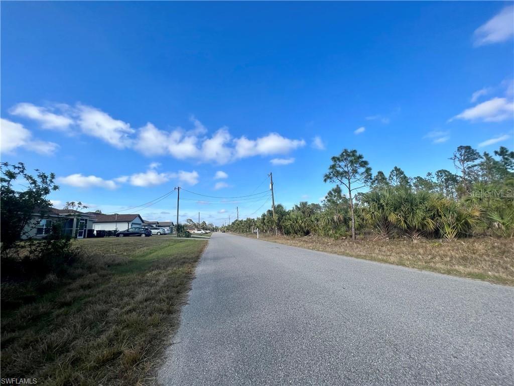 A paved road runs between a residential area and a wooded lot under a blue sky — Lot 30 KISKA ROAD, NORTH PORT, FL