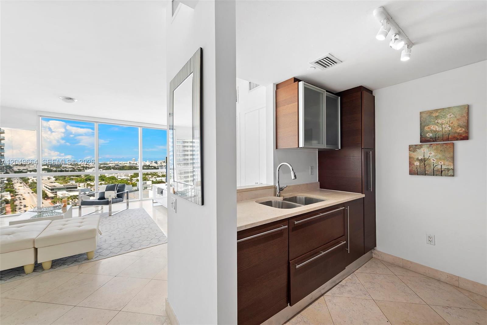 A kitchen with dark wood cabinets and stone countertops overlooks a bright living area — 450 Alton Rd # 1708, Miami Beach FL 33139, MIAMI BEACH, FL