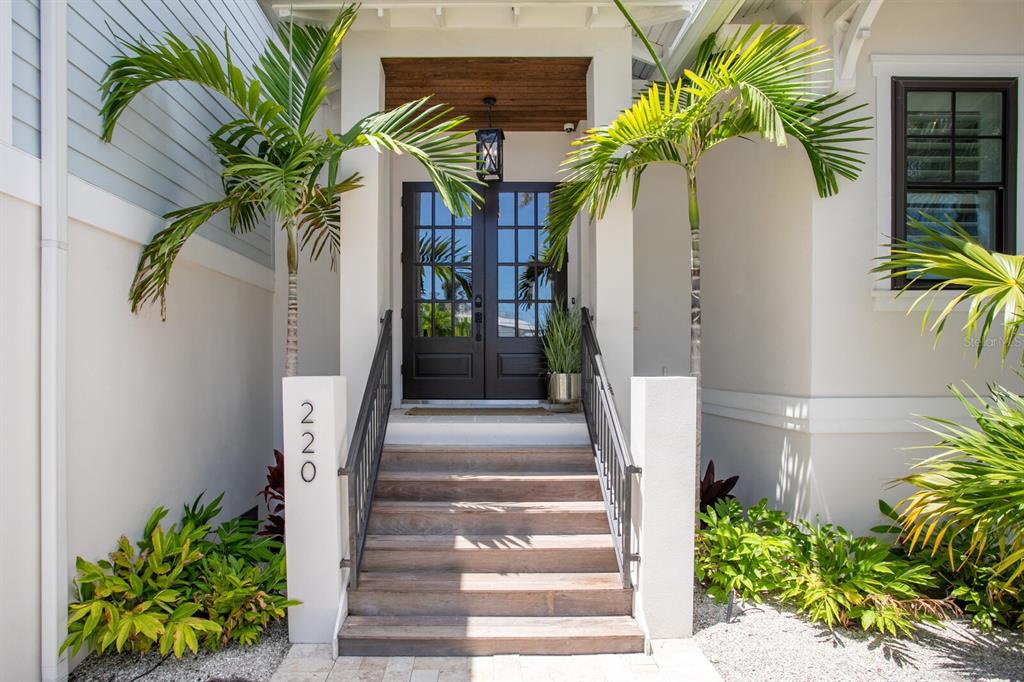 A front entrance features wooden stairs leading to double glass doors under a covered porch — 220 N HARBOR DRIVE, HOLMES BEACH, FL