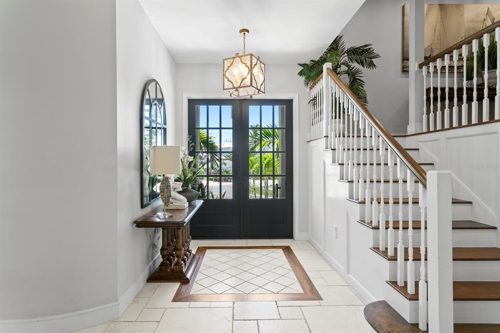 A bright foyer features a dark double door, a wooden console table, and a staircase — 220 N HARBOR DRIVE, HOLMES BEACH, FL