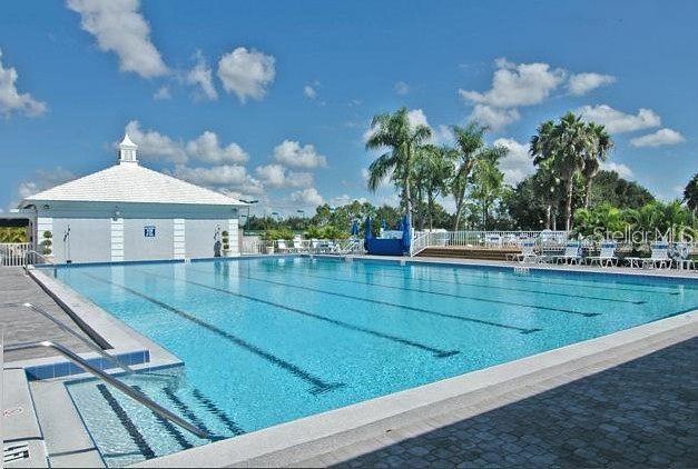 A large rectangular swimming pool with lap lanes sits beside a white building under blue skies — 314 CERROMAR WAY N UNIT 16, VENICE, FL