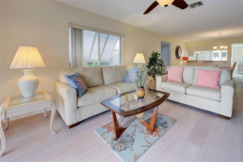 A living room features two beige sofas, a glass-topped coffee table, and light wood flooring — 314 CERROMAR WAY N UNIT 16, VENICE, FL