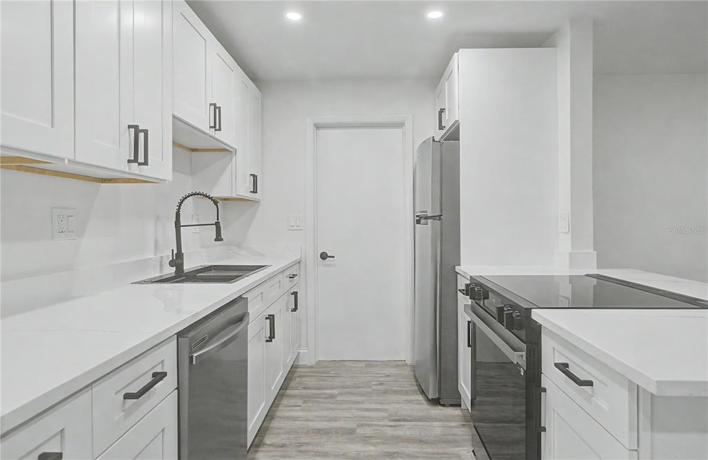 A modern kitchen features white cabinets, stainless steel appliances, and a dark faucet — 3 KANSAS STREET, BEVERLY HILLS, FL