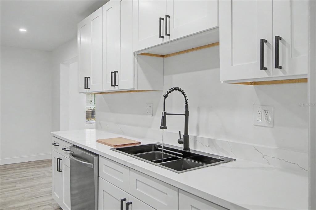 A modern kitchen features white shaker cabinets, a black faucet, and a stainless steel dishwasher — 3 KANSAS STREET, BEVERLY HILLS, FL