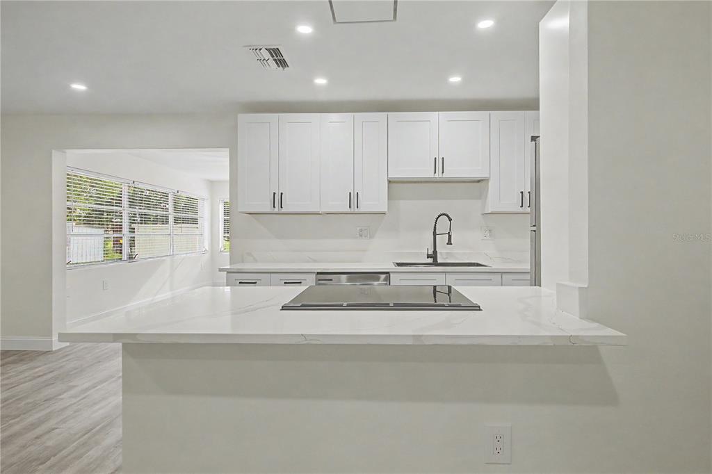 A modern kitchen features white cabinets, a marble-look island with a cooktop, and recessed lighting — 3 KANSAS STREET, BEVERLY HILLS, FL