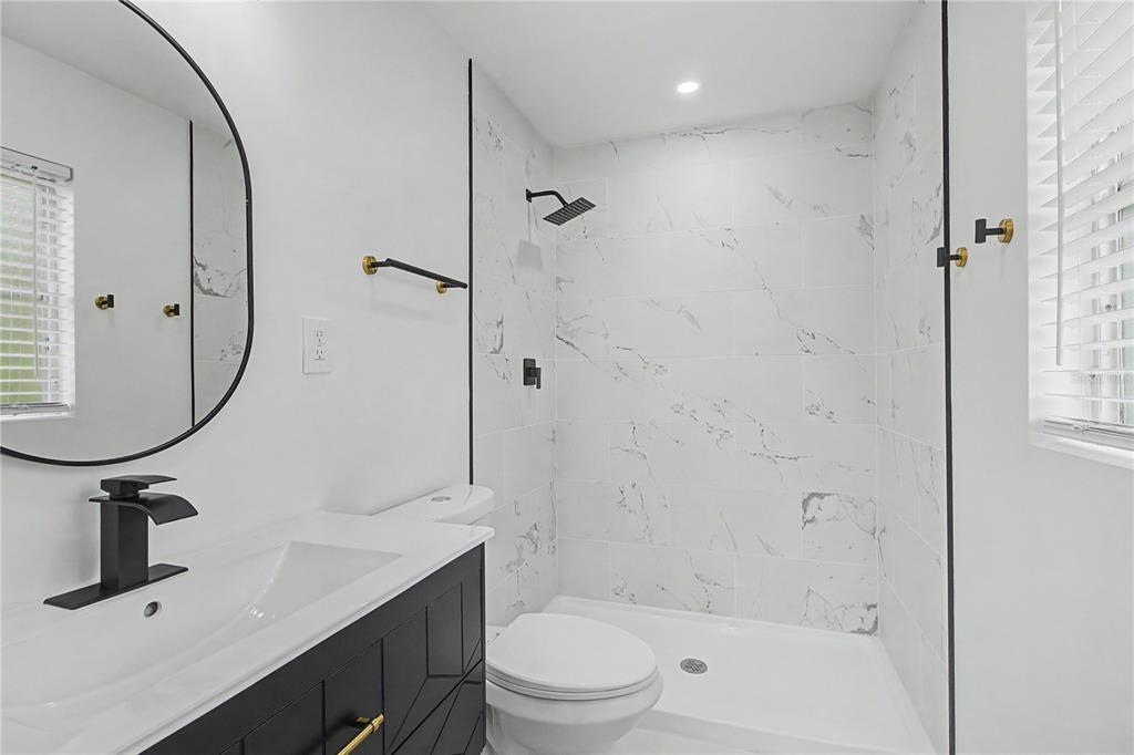 A modern bathroom features a black vanity, a round mirror, and a marble-tiled walk-in shower — 3 KANSAS STREET, BEVERLY HILLS, FL