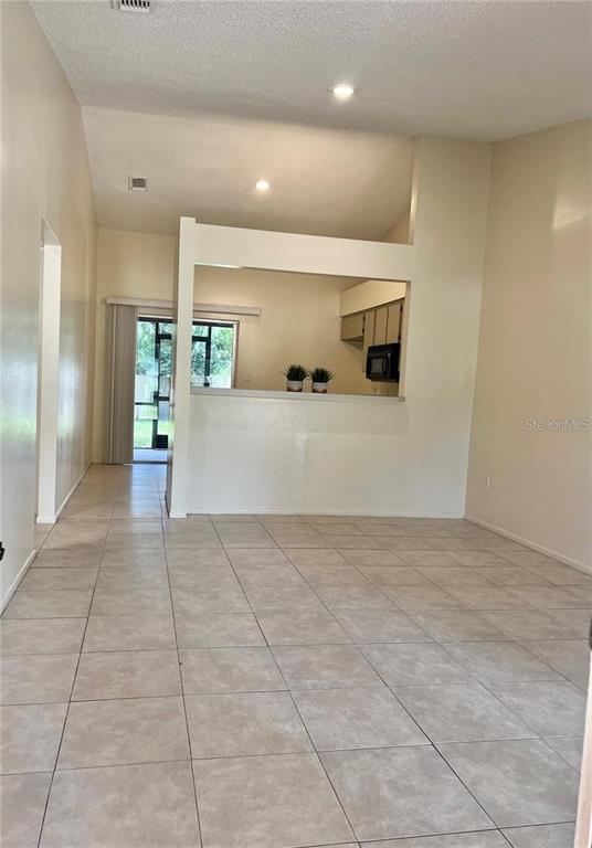 An open-concept living area features light-colored tile flooring and a pass-through window to the kitchen — 10376 RIVA RIDGE TRAIL, ORLANDO, FL