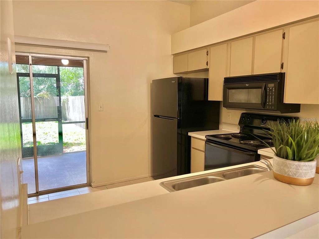 A kitchen features white countertops, beige cabinets, black appliances, and a sliding glass door — 10376 RIVA RIDGE TRAIL, ORLANDO, FL